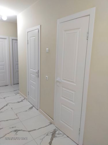 Установлена новая белая дверь, закреплены петли, ручка, замок, отрегулированы зазоры, выполнена отделка откосов, произведена чистовая отделка, проверена функциональность.