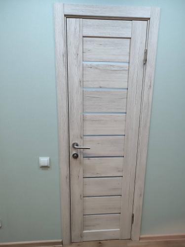 Установлена светлая дверь с ручкой и замком, закреплена в проеме, добавлены петли, наличники, отрегулирована по уровню, обеспечена плавная работа, завершен монтаж.