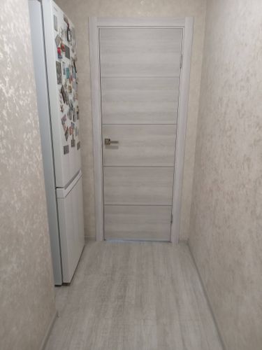 Установлена светлая дверь с горизонтальными линиями, аккуратно закреплена в проеме, добавлена фурнитура, обеспечивающая плавное открытие и закрытие. Завершена отделка откосов и наличников.