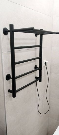 На стену ванной комнаты закреплено устройство для сушки полотенец, подключенное к электросети через розетку. Установлены крепления, обеспечивающие надежность и безопасность.