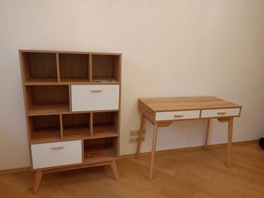 Собран деревянный стеллаж с полками и выдвижными ящиками. Установлены крепления, обеспечена устойчивость конструкции. Рядом размещен стол с двумя ящиками, выполненный в едином стиле.