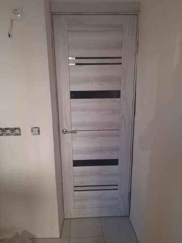 Установлена новая створка, закреплены петли, врезан замок, ручка прикреплена. Коробка выровнена, зазоры устранены, наличники смонтированы, конструкция проверена на плавность открывания.