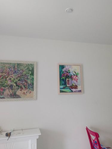 На стене закреплены два живописных полотна в рамах, одно из которых изображает цветы. Пространство оформлено с использованием инструментов, оставленных на белой поверхности.