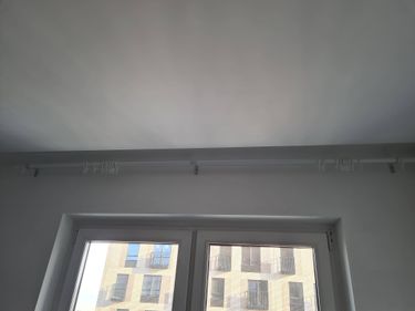 Установлен потолочный карниз для штор над окном, закреплённый на стене. Комплект крючков готов к использованию. Работа завершена аккуратно и надежно.