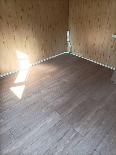 В комнате уложено новое напольное покрытие. Панели аккуратно состыкованы, создавая ровную поверхность. Углы и стыки обработаны, обеспечивая эстетичный вид и долговечность.