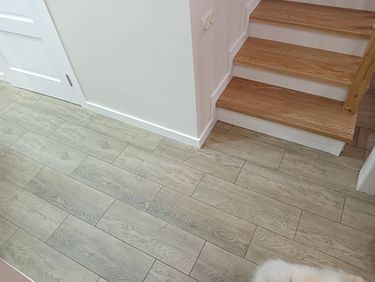 Установлены белоснежные плинтусы вдоль стены и лестницы, аккуратно прилегающие к светлому ламинату. Завершено оформление стыков и углов, обеспечивая гармоничный переход между поверхностями.