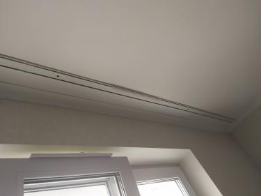 Закреплен потолочный профиль для штор над окном, выполнены отверстия, установлены крепежные элементы, обеспечена надежная фиксация конструкции, завершена работа по монтажу.