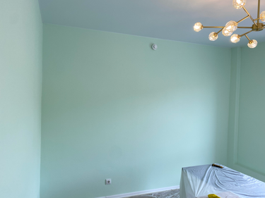 Стены покрыты свежим слоем краски нежного мятного оттенка, создавая светлую и уютную атмосферу в помещении. Потолок и углы аккуратно обработаны, мебель защищена пленкой.