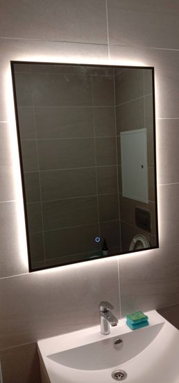 Установлено зеркало с подсветкой в ванной комнате. Светодиодная лента интегрирована по периметру, обеспечивая равномерное освещение. Завершён монтаж сантехники, включая раковину и смеситель.