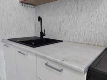 Установлена новая столешница из ДСП, вырезано отверстие под мойку, закреплены края, подключен смеситель, проверена герметичность соединений, завершена отделка поверхности.