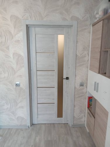 Установлена новая деревянная дверь с фурнитурой, отрегулированы петли, закреплён наличник, проверена плавность закрытия, обеспечена звукоизоляция, завершена отделка проёма.