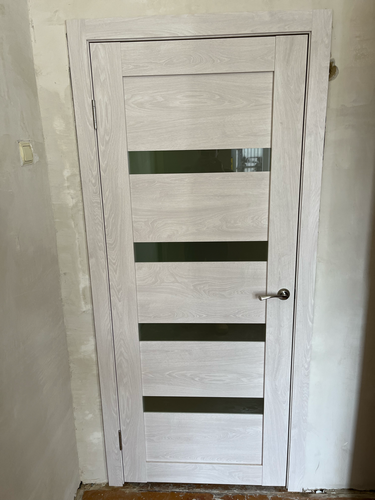 Установлена светлая дверь с горизонтальными стеклянными вставками, закреплена фурнитура, отрегулированы петли, обеспечена плавная работа, завершена отделка проема.