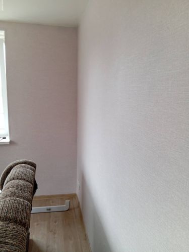 На стенах ровно наклеены обои светлого оттенка, без видимых швов и пузырей. Поверхность гладкая, углы аккуратно обработаны, создавая завершенный и опрятный вид интерьера.