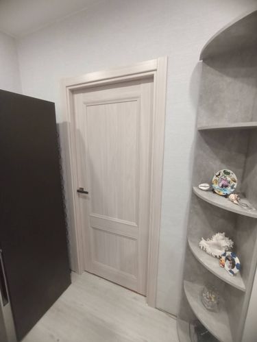 Установлена светлая дверь с ручкой, выполнена подгонка коробки, закреплены петли, произведена регулировка полотна, обеспечена плавная работа, добавлены наличники для завершённого вида.