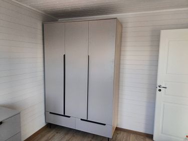 Собран шкаф с дверцами и ящиками. Установлены ручки, закреплены петли, выровнены панели. Проверена устойчивость и функциональность. Размещён в углу комнаты, готов к использованию.