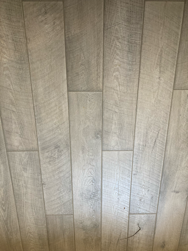 На ровное основание уложены панели, образующие гладкую поверхность с текстурой дерева. Швы плотно соединены, создавая единый рисунок, без зазоров и неровностей.