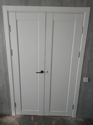 Установлена белая дверь с двумя створками, закреплены петли, врезана ручка, отрегулированы зазоры, добавлены наличники, произведена проверка плавности открывания и закрывания.