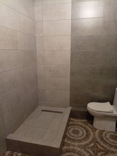 Завершена облицовка стен и пола керамогранитом в ванной комнате. Плитка уложена ровно, стыки аккуратные, швы затерты. Душевой поддон облицован, установлен слив.