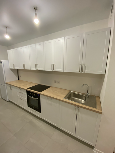 Установлены шкафы, смонтирована столешница, врезана мойка, подключена варочная панель, размещены ручки, отрегулированы фасады, подключены светильники.