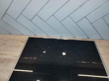 Уложена плитка на стену в виде "елочки", установлена варочная панель на кухонную поверхность. Завершено оформление рабочей зоны.