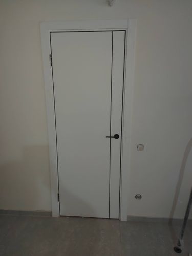 Установлена белая межкомнатная дверь с ручкой и петлями. Коробка закреплена, зазоры выровнены, конструкция надежно зафиксирована в проеме, обеспечена плавная работа створки.