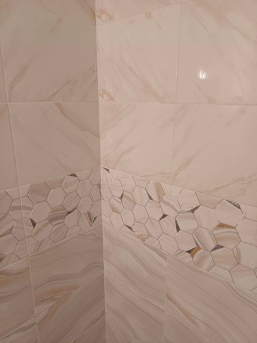 Завершена облицовка стен керамогранитом с мраморным узором. Вставка из шестиугольной мозаики добавляет акцент. Поверхность ровная, швы аккуратные, гармоничное сочетание текстур.