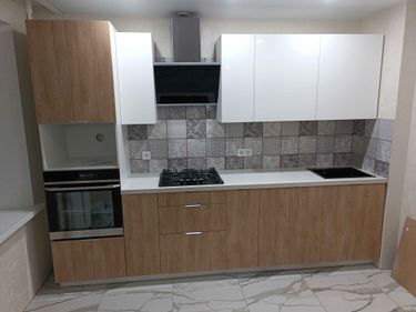 Установлены шкафы, закреплены фасады, смонтирована столешница, подключены варочная панель и духовой шкаф, установлена вытяжка, выполнена облицовка стены плиткой.