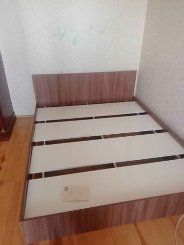 Собрана двуспальная кровать: установлены боковые панели, закреплено изголовье, уложены ламели. Все детали надежно соединены, конструкция устойчива. Инструкция использована для точности.