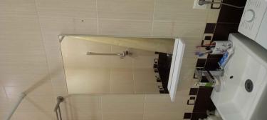 Зеркало надежно закреплено на стене ванной комнаты. Установлено ровно, без перекосов, с учетом уровня. Под ним размещена полка для удобства хранения мелочей.