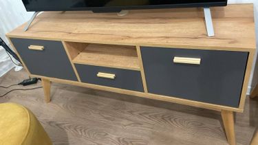 Собран деревянный шкаф с полками и ящиками, установлены дверцы и ручки, конструкция стоит на ножках, готова к использованию.