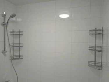 Изображение ванной комнаты с белой плиткой и полками. Установлены душ и светильник. Работа завершена, все элементы на своих местах, аккуратная отделка.