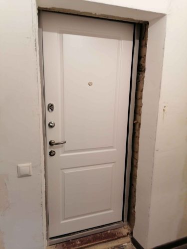 Установлена новая белая дверь с глазком и замками, произведена отделка проема, обеспечена надежная фиксация конструкции, улучшена звукоизоляция и внешний вид входной зоны.