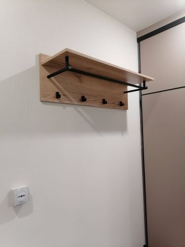 На стене закреплена деревянная панель с металлическими крючками и полкой. Конструкция надежно установлена, обеспечивая удобное хранение одежды и аксессуаров.