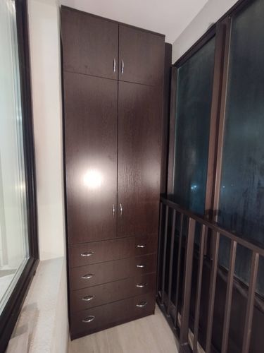 Собран высокий шкаф с дверцами и ящиками, установлен в углу комнаты. Все элементы плотно соединены, ручки прикреплены. Конструкция устойчива, занимает минимальное пространство.