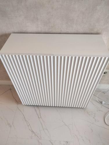 Собран белый комод с рельефными дверцами, установлен на ровный пол. Все детали тщательно соединены, конструкция устойчива и готова к использованию.