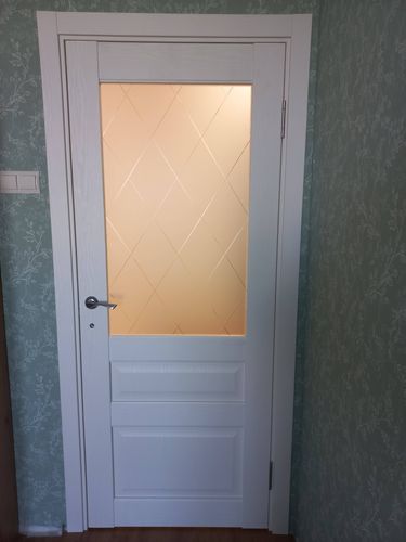 Установлена белая дверь с матовым стеклом, смонтированы петли, ручка и замок. Коробка закреплена в проеме, наличники подогнаны, обеспечена плавная работа конструкции.