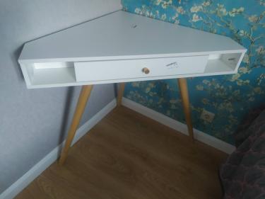 Собрано угловое белое изделие с деревянными ножками и выдвижным ящиком. Установлено в угол комнаты, обеспечивая устойчивость и функциональность.