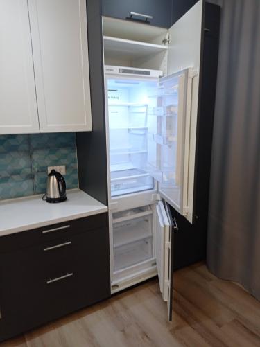 Встроенный холодильник аккуратно размещён в нише, подключён к электросети, дверцы выровнены, обеспечена плотная посадка, проверена функциональность, установлены декоративные панели.