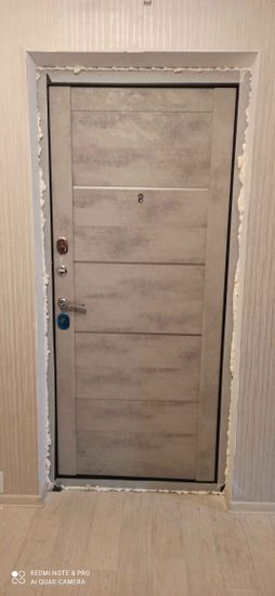 Установлена новая дверь, закреплена в проеме, зазоры заполнены монтажной пеной, обеспечена надежная фиксация и плотное прилегание. Завершены отделочные работы вокруг конструкции.