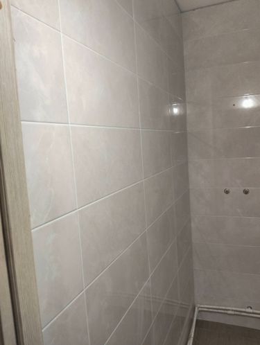 Стены ванной облицованы светлой керамикой, швы аккуратно заделаны, поверхность ровная и гладкая, создавая современный и чистый вид.