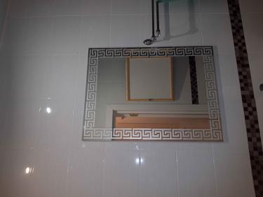 Зеркало с узорной рамкой аккуратно закреплено на стене ванной комнаты, ровно выровнено, надежно зафиксировано, отражает свет, создавая ощущение простора и завершенности интерьера.