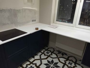 Установлена белая столешница, подогнана по размерам, вырезаны отверстия для варочной панели. Поверхность закреплена на кухонные шкафы, обеспечивая прочность и устойчивость.