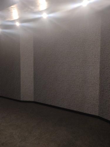 На полу уложены плитки ковролина, создающие ровное покрытие. Завершенная работа обеспечивает комфорт и эстетичность помещения. Светильники на потолке подчеркивают текстуру стен и пола.