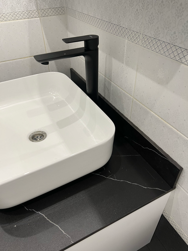 Установлена раковина на черной столешнице, подключен смеситель, выполнены все необходимые соединения для водоснабжения и слива, обеспечена герметизация, проверена функциональность системы.