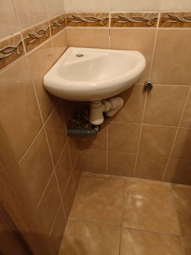 Установлен угловой умывальник, подключены трубы для подачи холодной и горячей воды, смонтирован слив. Все элементы аккуратно интегрированы в интерьер ванной комнаты.