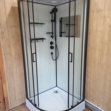 Установлена современная душевая кабина с прозрачными дверями и черными элементами. Выполнен монтаж сливной системы, подключены водопроводные коммуникации, добавлены полки для удобства.