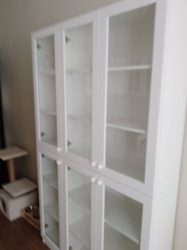Собран белый шкаф с четырьмя стеклянными дверцами, установлен на ровную поверхность. Внутри размещены полки для хранения. Работа выполнена аккуратно, конструкция устойчива.