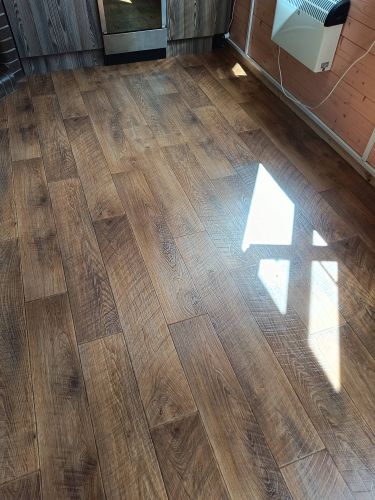 На подготовленное основание уложено новое покрытие, тщательно выровненное и закрепленное без зазоров, создающее эффект деревянного пола. Завершён монтаж с аккуратной подгонкой по краям.