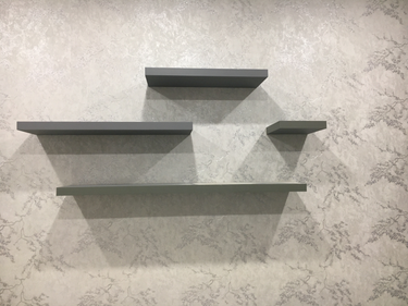 На стене закреплены четыре полки разного размера, расположенные асимметрично. Установка завершена, элементы надежно зафиксированы, создавая функциональное и эстетичное пространство.