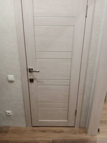 Установлена новая створка, закреплены петли, врезан замок, ручка на месте, отрегулированы зазоры, проверена плавность хода, завершена отделка проема, обеспечена надежная фиксация.